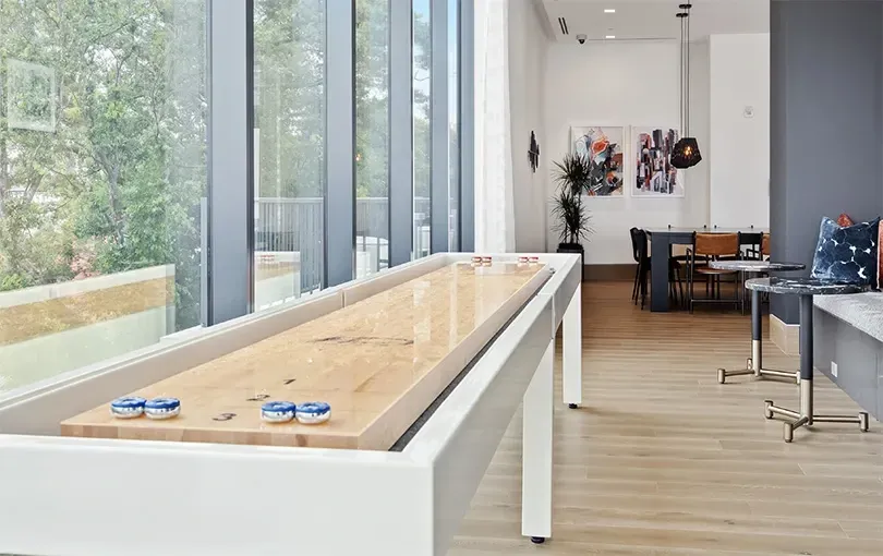 Shuffleboard table in a modern community lounge with large windows.