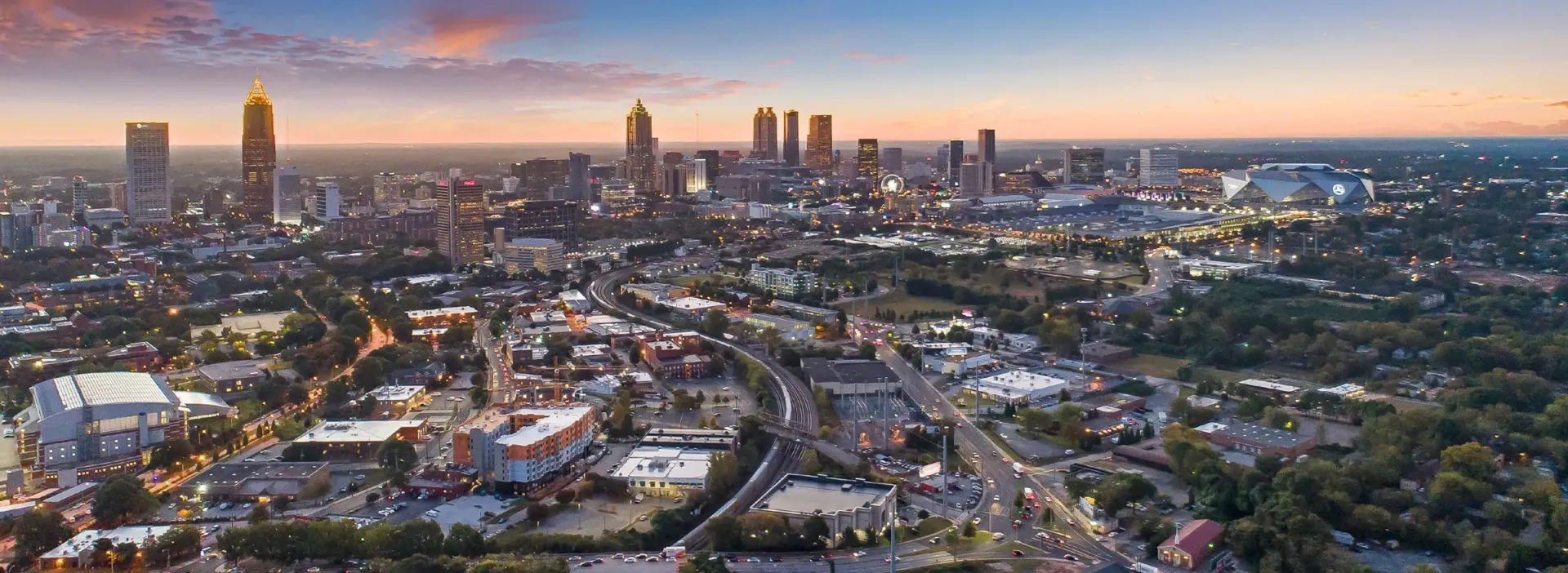 Aerial view of a sprawling city skyline at dusk, showcasing skyscrapers, highways, and a stadium.