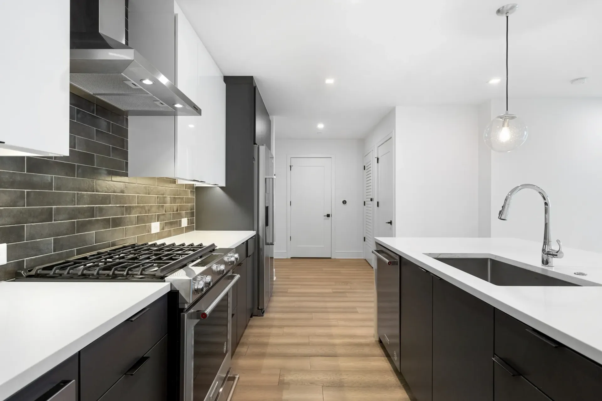 Modern kitchen with stainless steel appliances, gas range, dark cabinets, and white countertops.