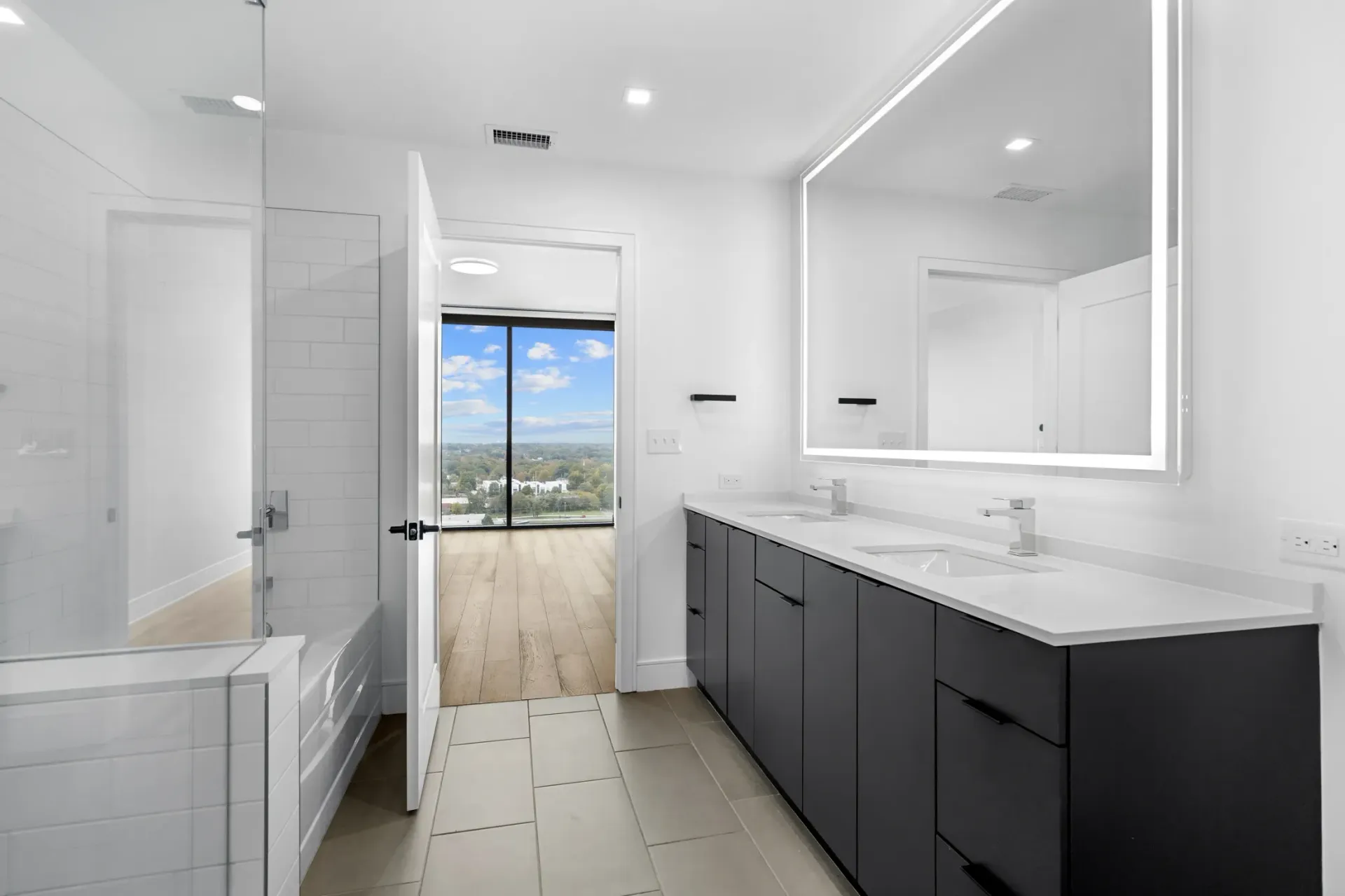 Modern bathroom with dual vanity, large illuminated mirror, and glass-enclosed shower.