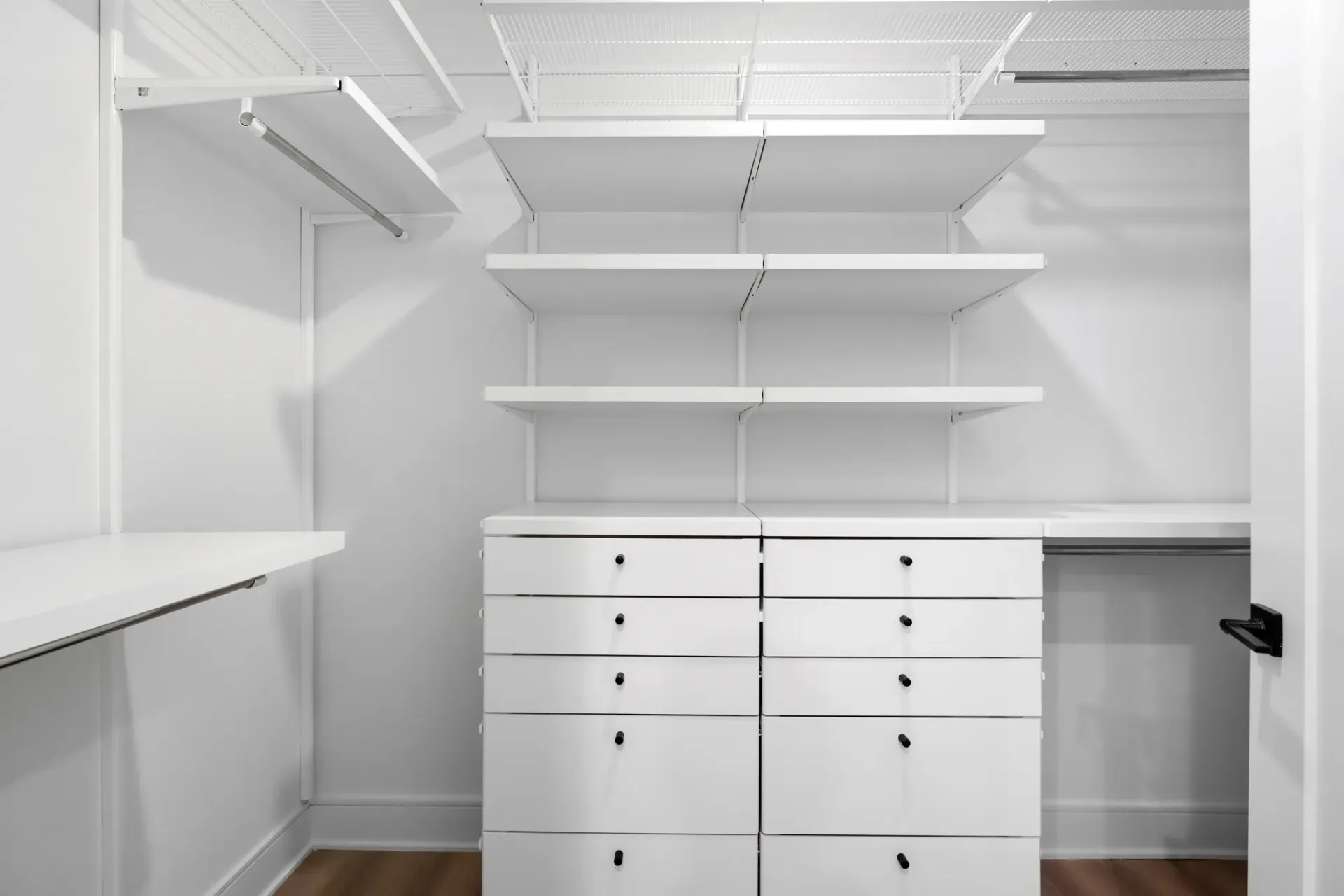 Empty walk-in closet with white shelving and drawers.