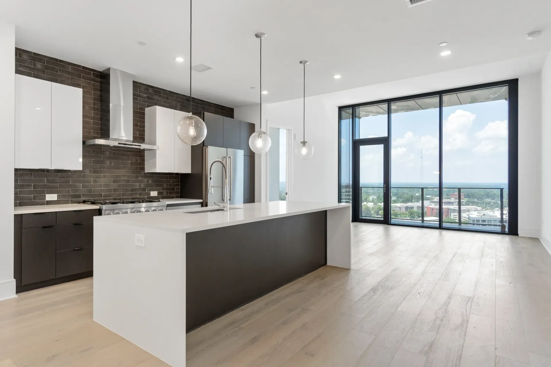 Modern kitchen with island and stainless steel appliances, large windows with city view.