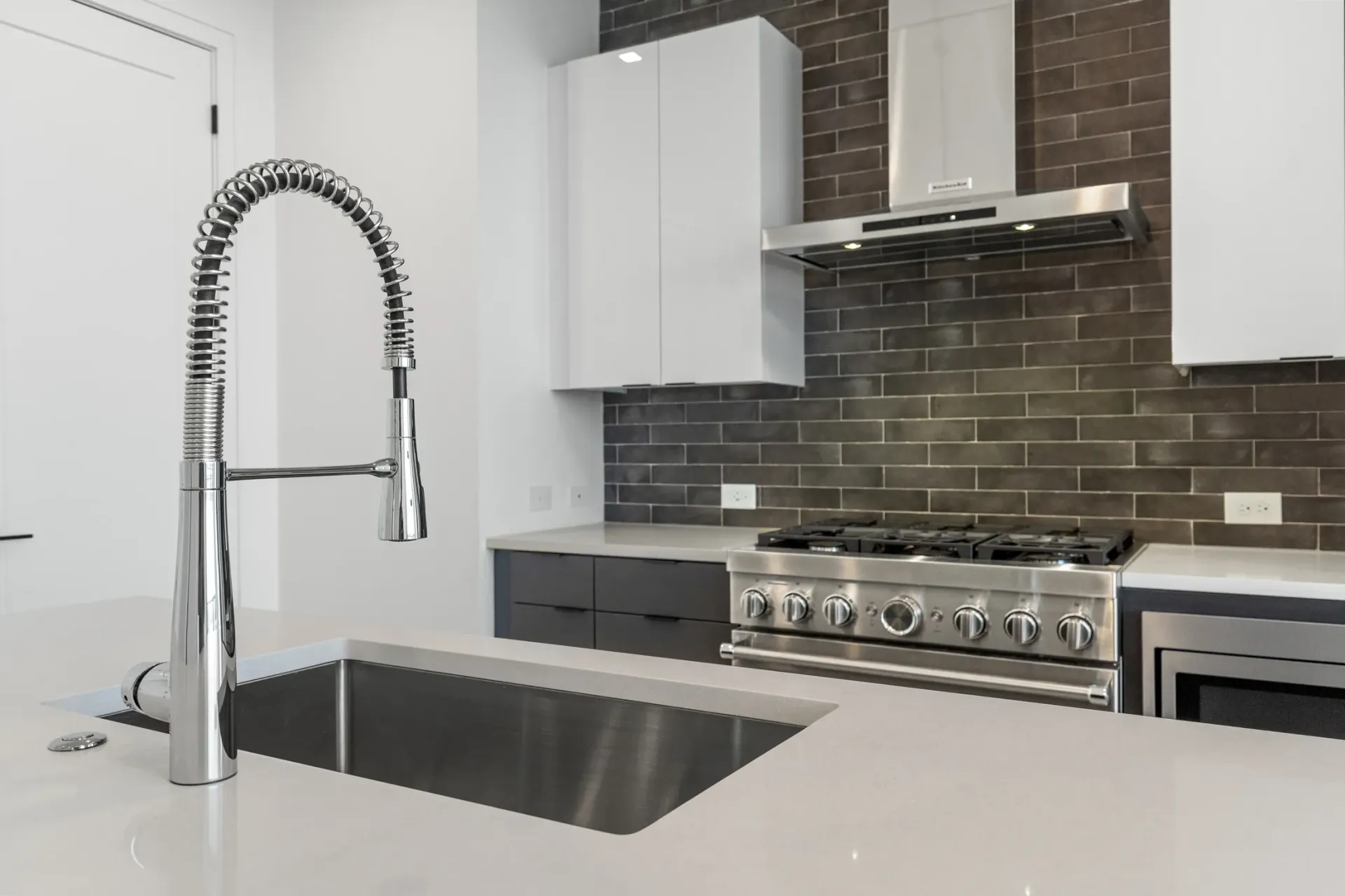 Modern kitchen with stainless steel appliances, quartz countertops, and a large sink with a coil faucet.