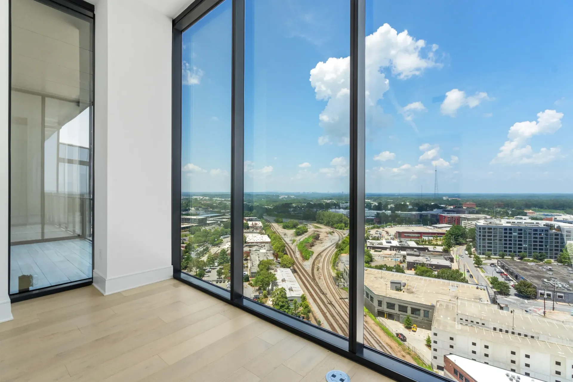 View from a high-rise apartment window overlooking a city with train tracks and buildings under a blue sky with clouds.