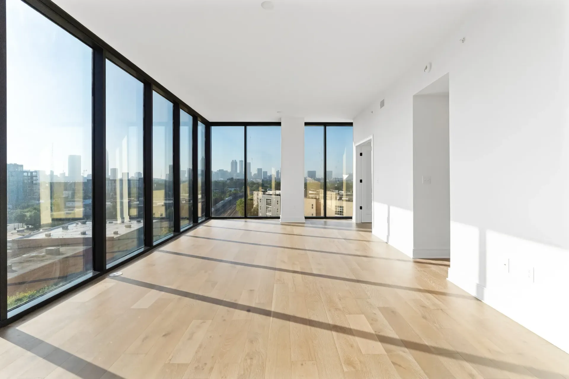 Empty apartment living area with floor-to-ceiling windows and city views.