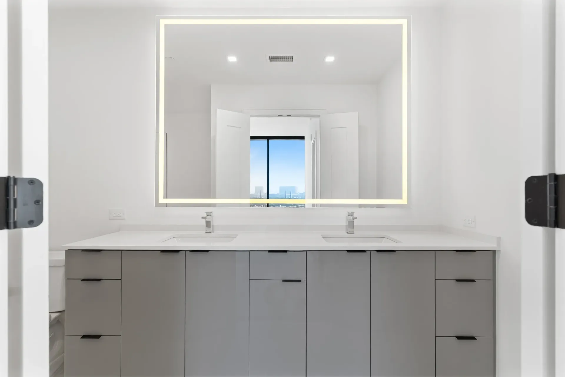 Modern bathroom with double vanity, illuminated mirror, and city view.