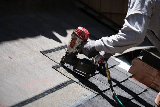 Roofer using a nail gun to install asphalt shingles on a roof.