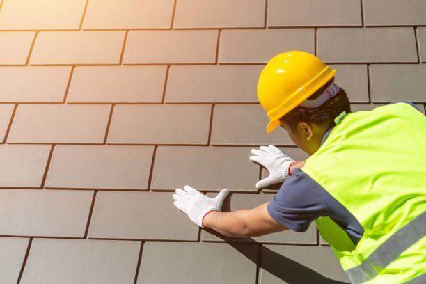 Construction worker in yellow helmet and safety vest installing roof tiles.