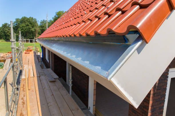 New roof with red tiles and silver gutters on a brick building with construction scaffolding.