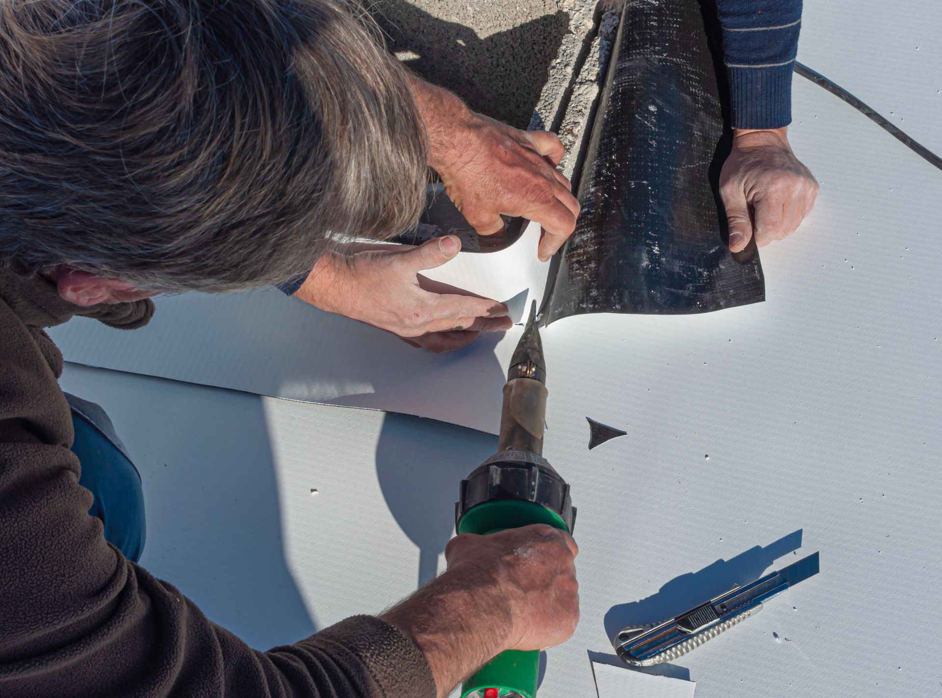 Two people welding a black membrane to a white surface, using a heat gun.