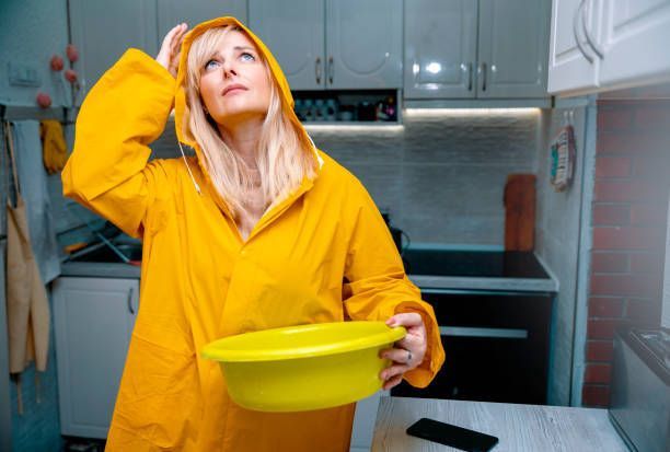 Woman in yellow raincoat looks up at ceiling, holding a yellow bowl in a kitchen.
