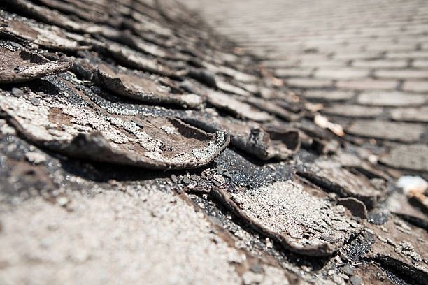 Close-up view of old, weathered asphalt shingles on a roof, showing deterioration and peeling.
