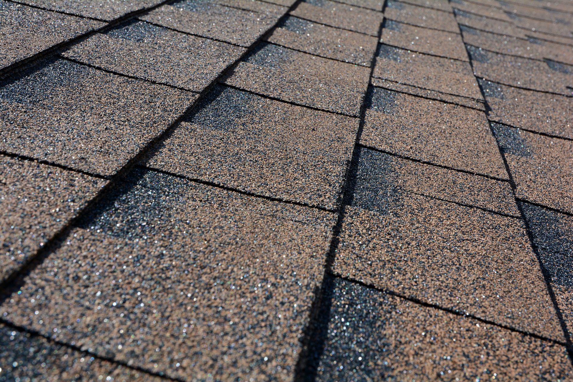 Close-up of brown and black asphalt roof shingles on a sloping roof.
