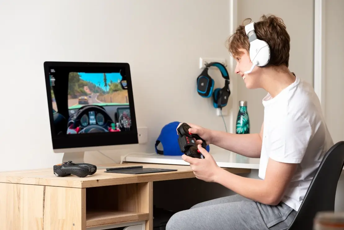 A young man wearing headphones is playing a video game on a computer.
