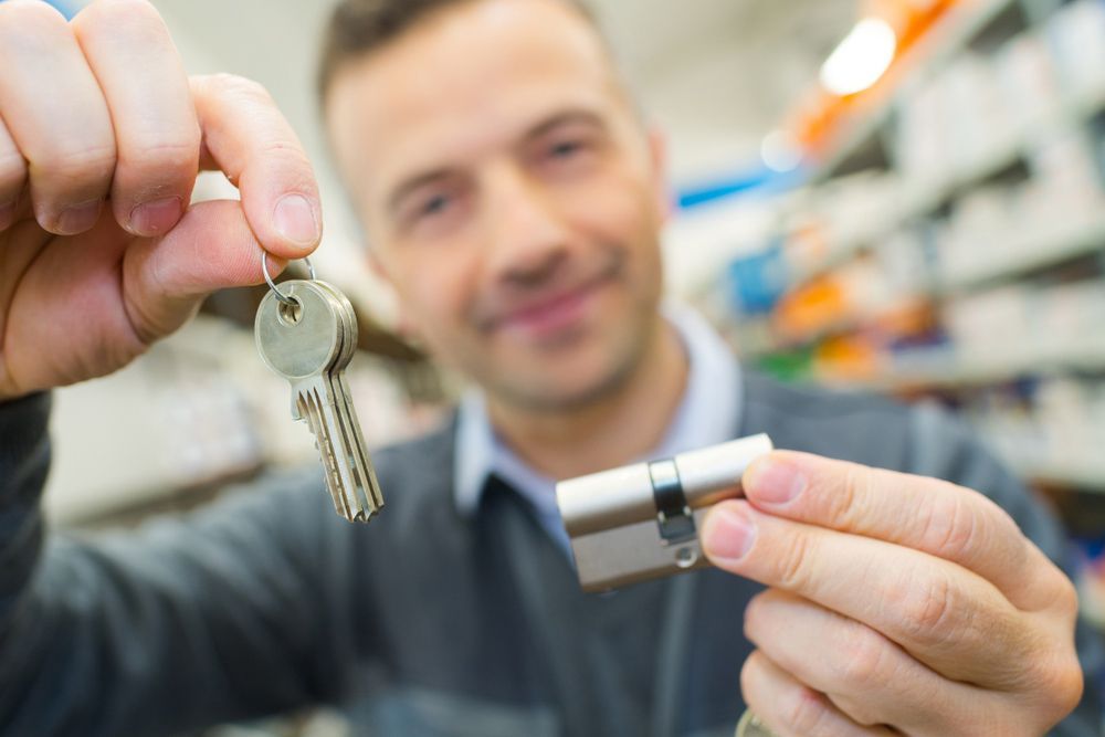 A Man Is Holding A Key And A Key Cylinder In His Hands — Eddie Williams Locksmiths in Cairns City, QLD