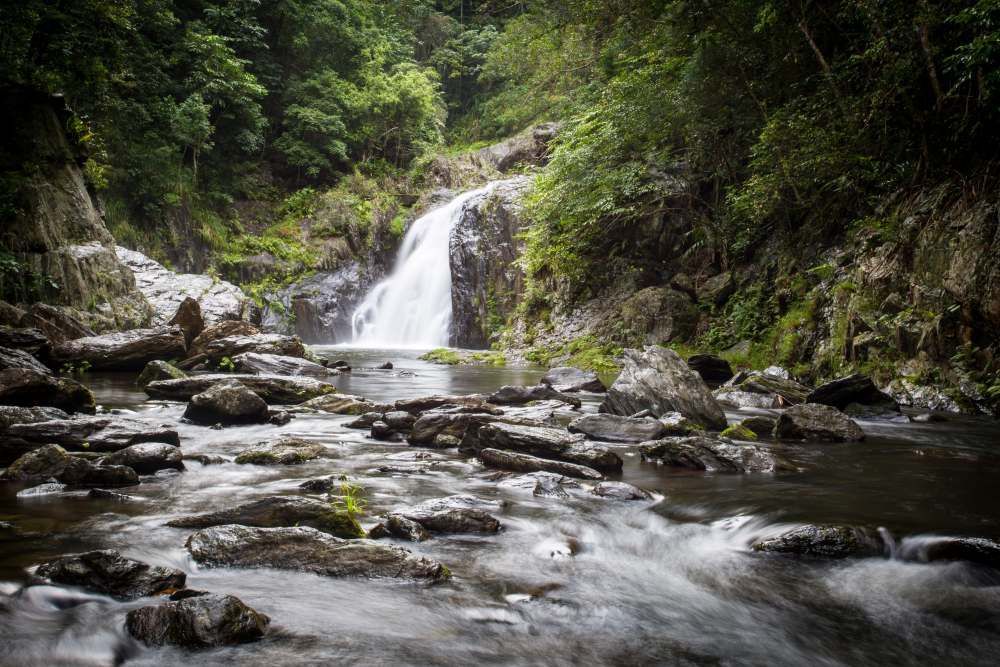 A Waterfall is Surrounded by Trees and Rocks in the Middle of a River — Eddie Williams Locksmiths in Redlynch, QLD