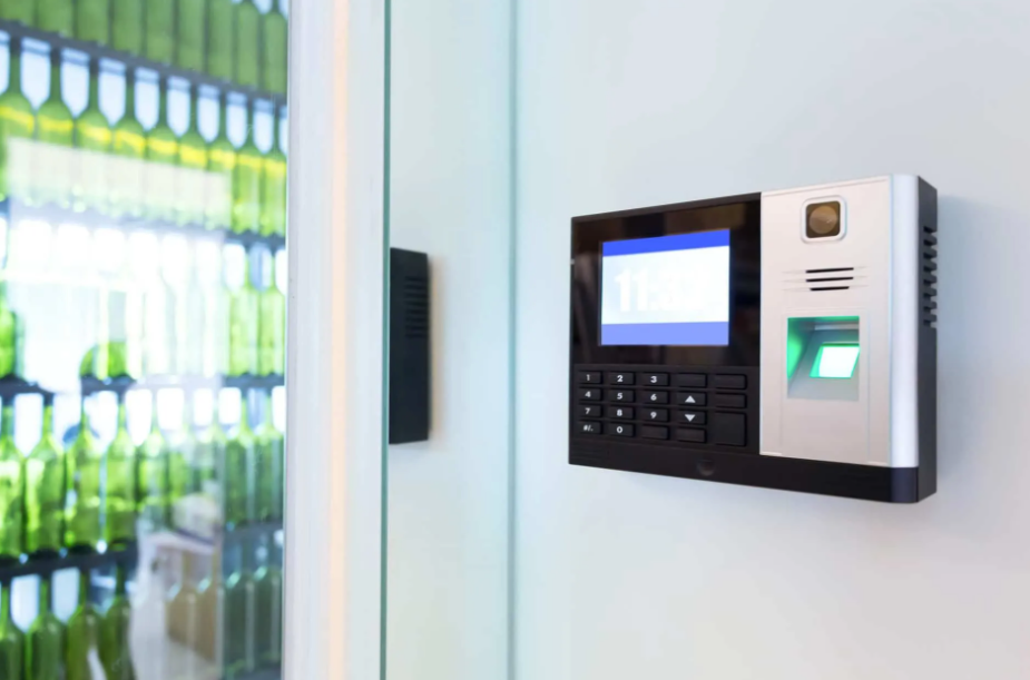 A biometric fingerprint scanner and keypad mounted on a wall next to a glass wall displaying rows of green wine bottles.