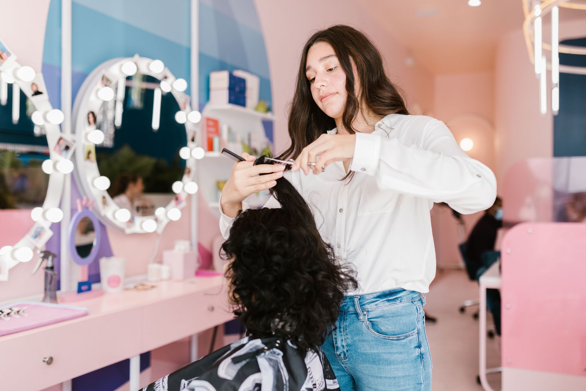 Stylist cutting curly hair in a pink salon near a vanity mirror