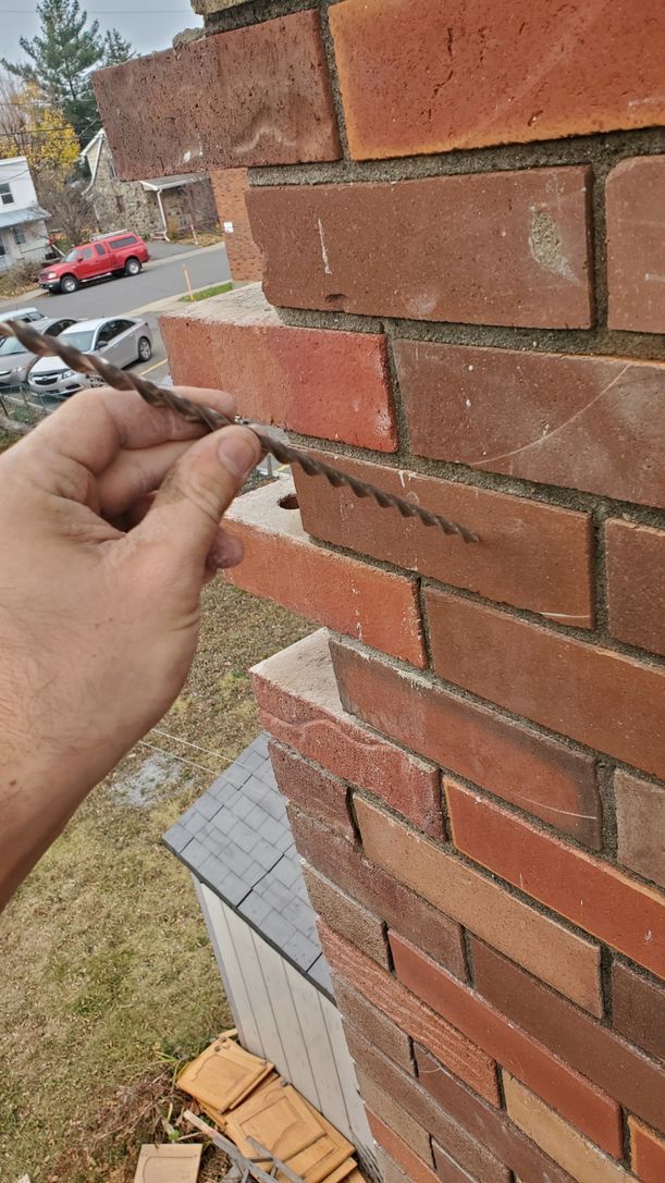 Une personne tient un morceau de bois devant un mur de briques.