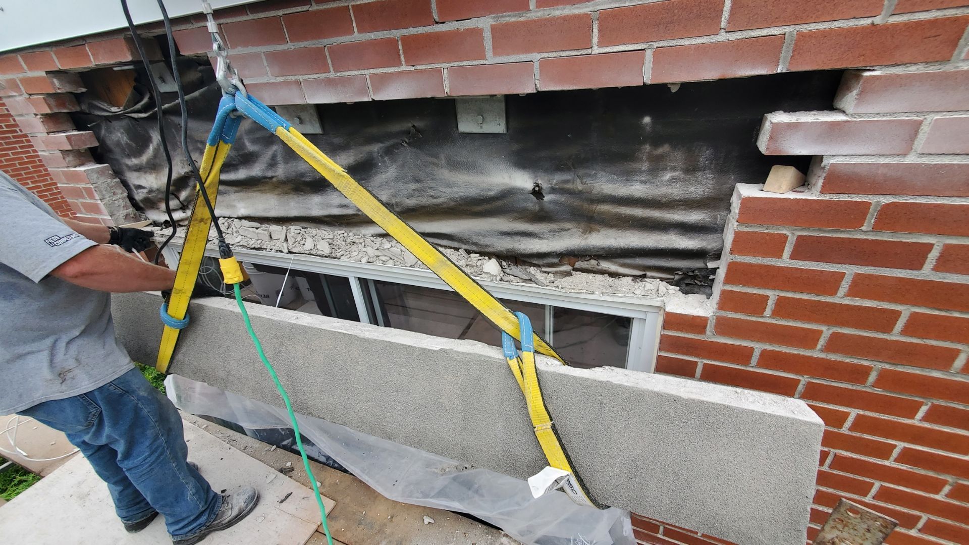 Un homme travaille sur un mur de briques avec une élingue attachée dessus.