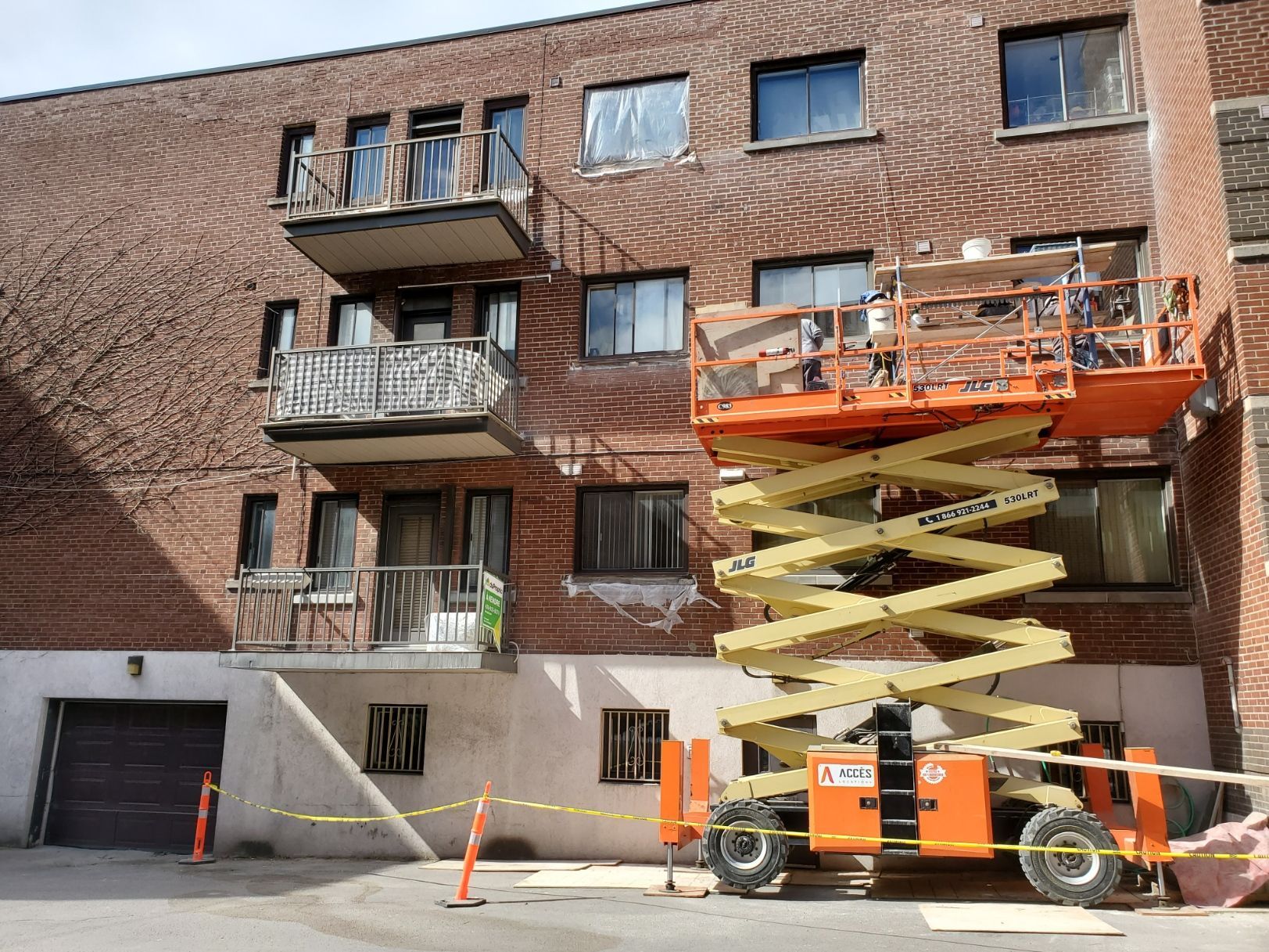 Un élévateur à ciseaux est garé devant un bâtiment en briques.