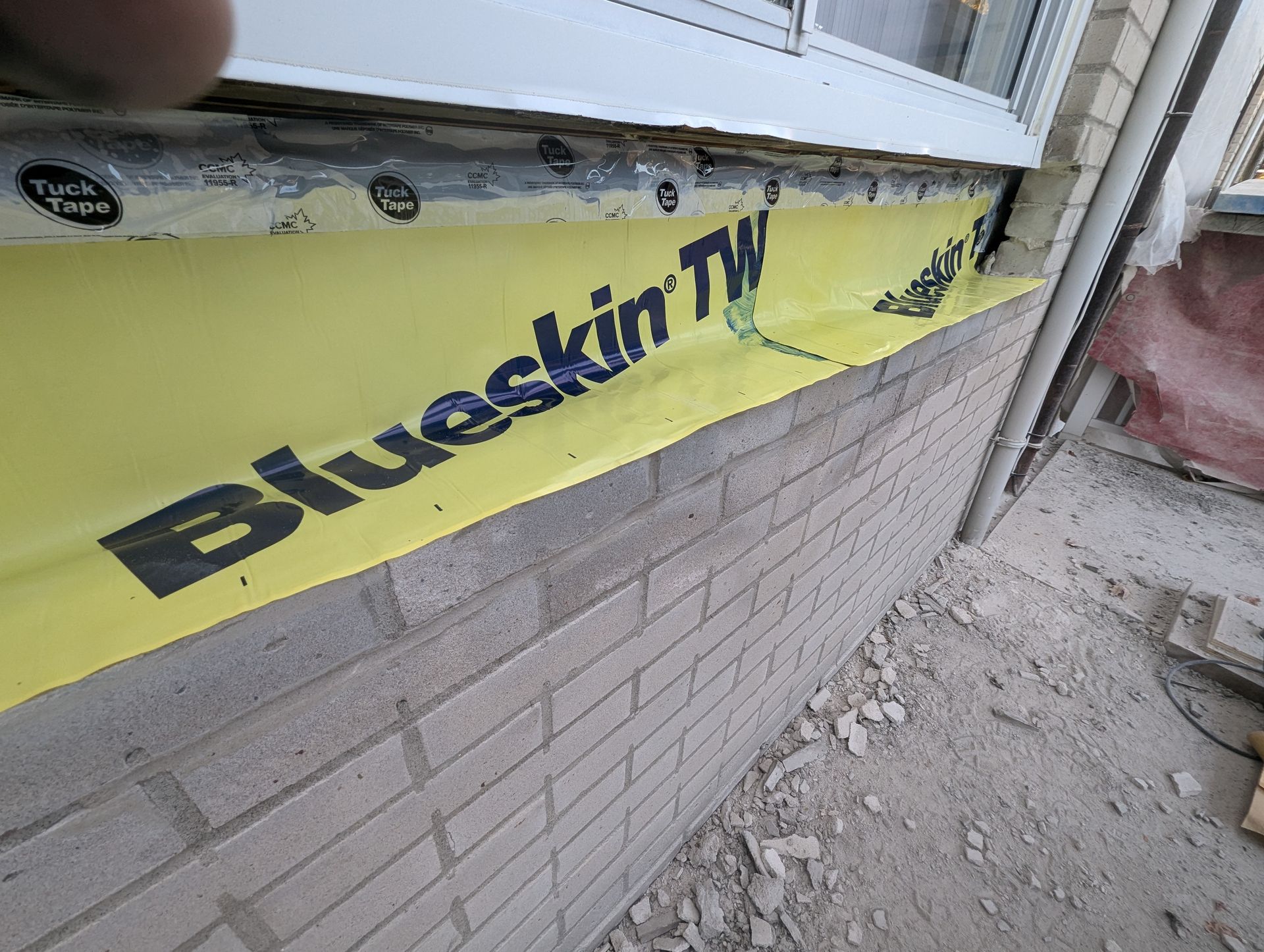 Une personne tient un ruban adhésif bleu jaune sur un mur de briques.