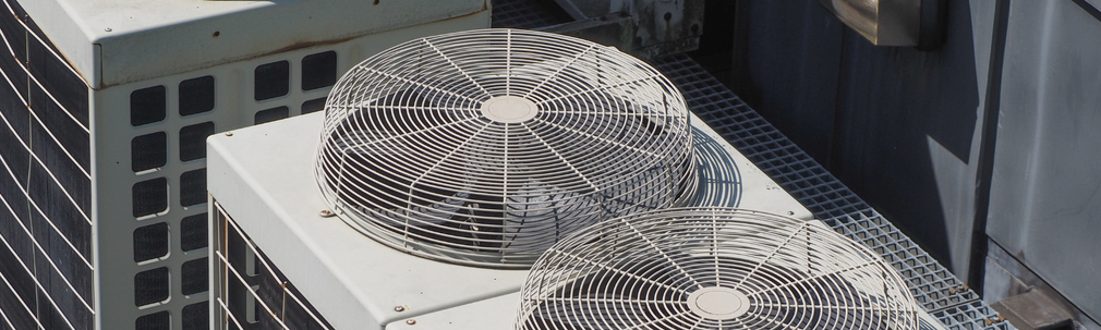 Two large rooftop air-conditioning fans on a white building beside tall dark office towers
