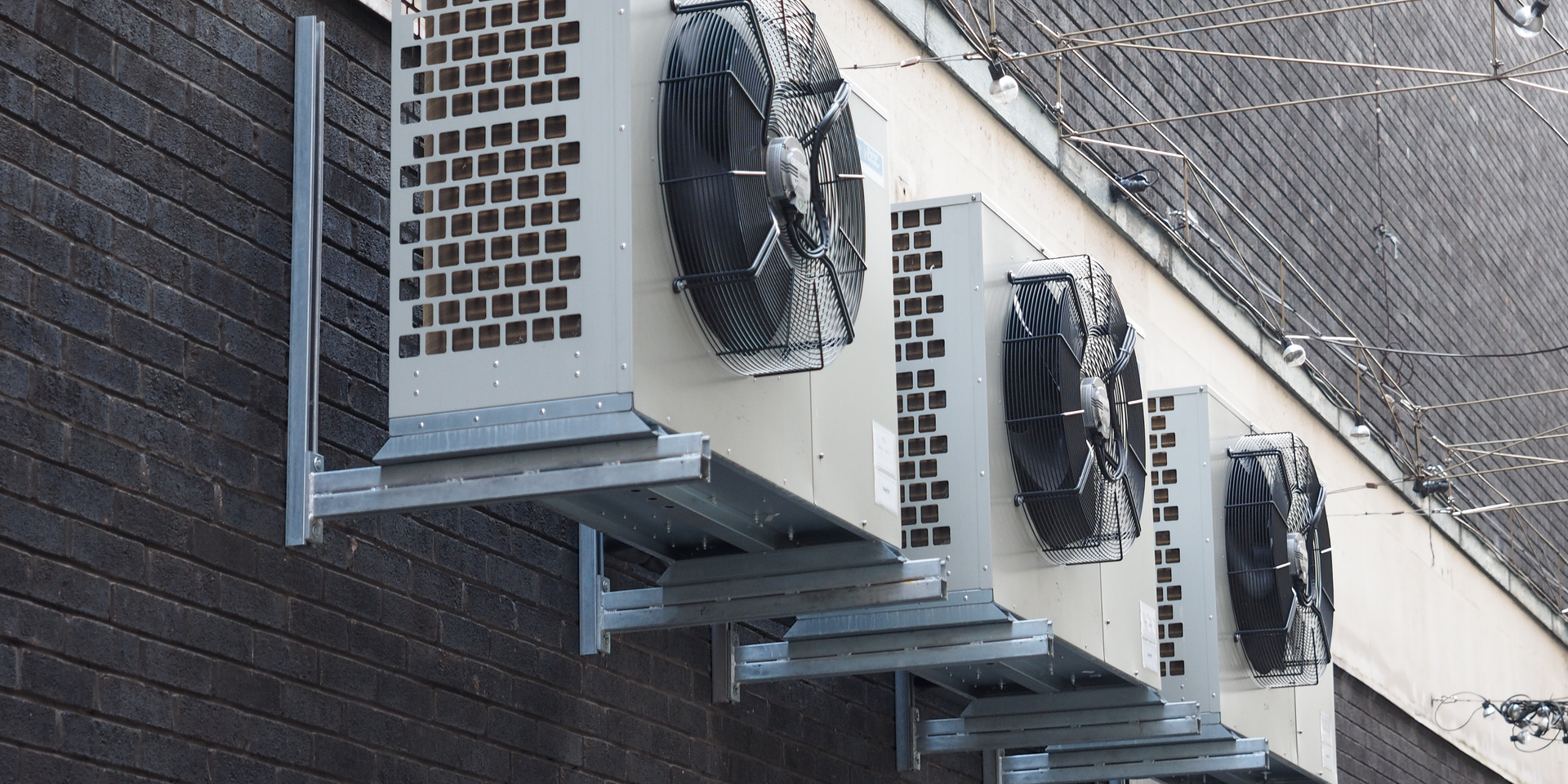 Row of outdoor air conditioning units mounted on a building wall under a sloped roof