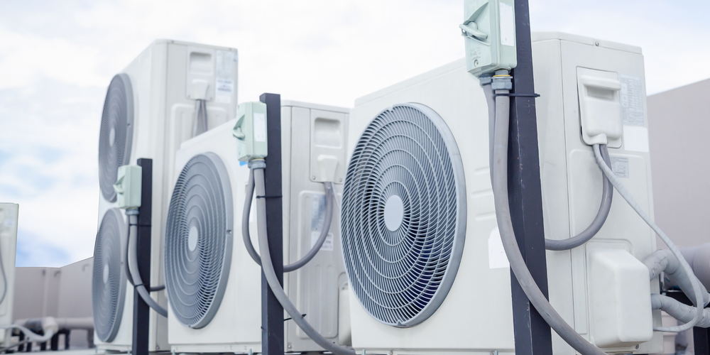 Outdoor row of white air conditioning units with large circular fans on a rooftop or exterior wall