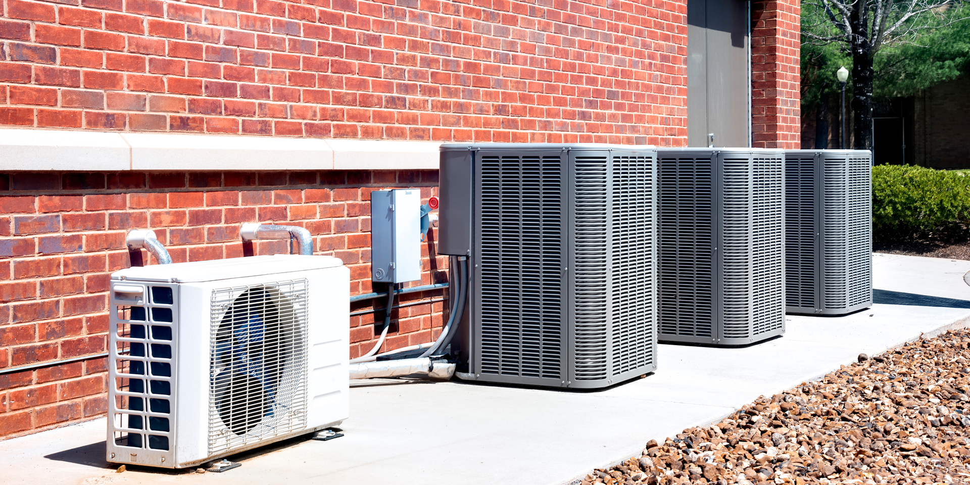 Air conditioning units lined up beside a brick building on a rooftop or exterior utility area