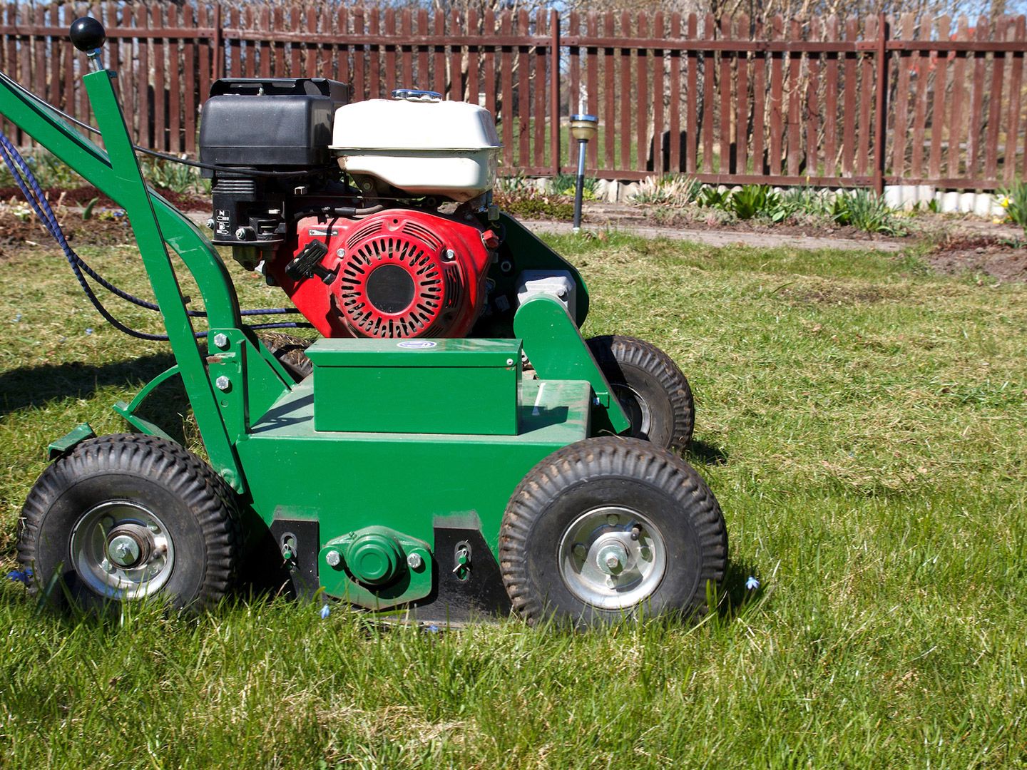 Green lawn aerator with a red and black engine, on a grassy lawn.