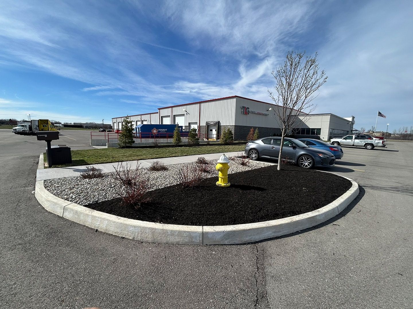 Exterior of a business building with cars parked nearby, landscaping, and a blue sky.