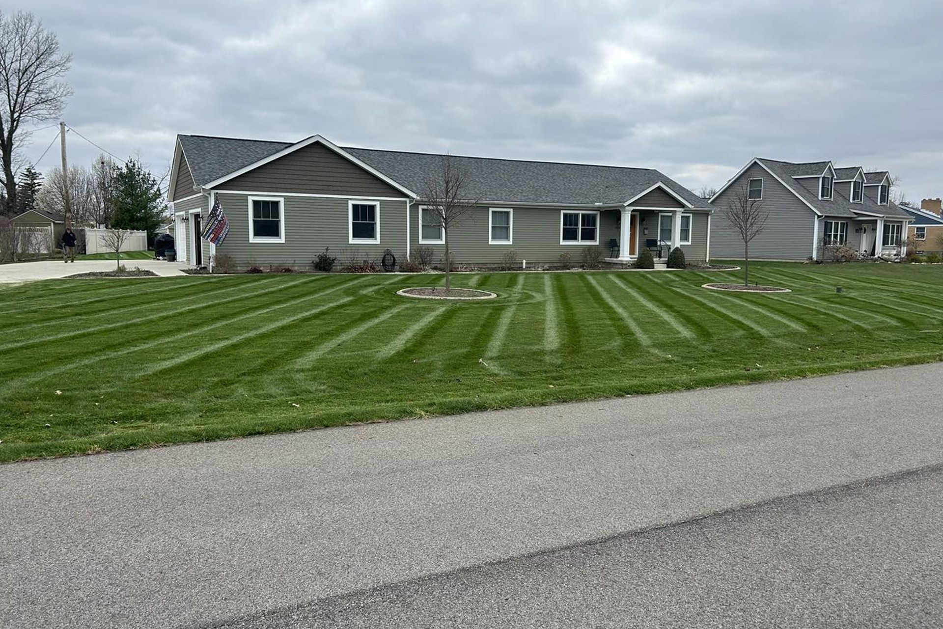 Green lawn with freshly cut stripes in front of a gray house on a cloudy day.