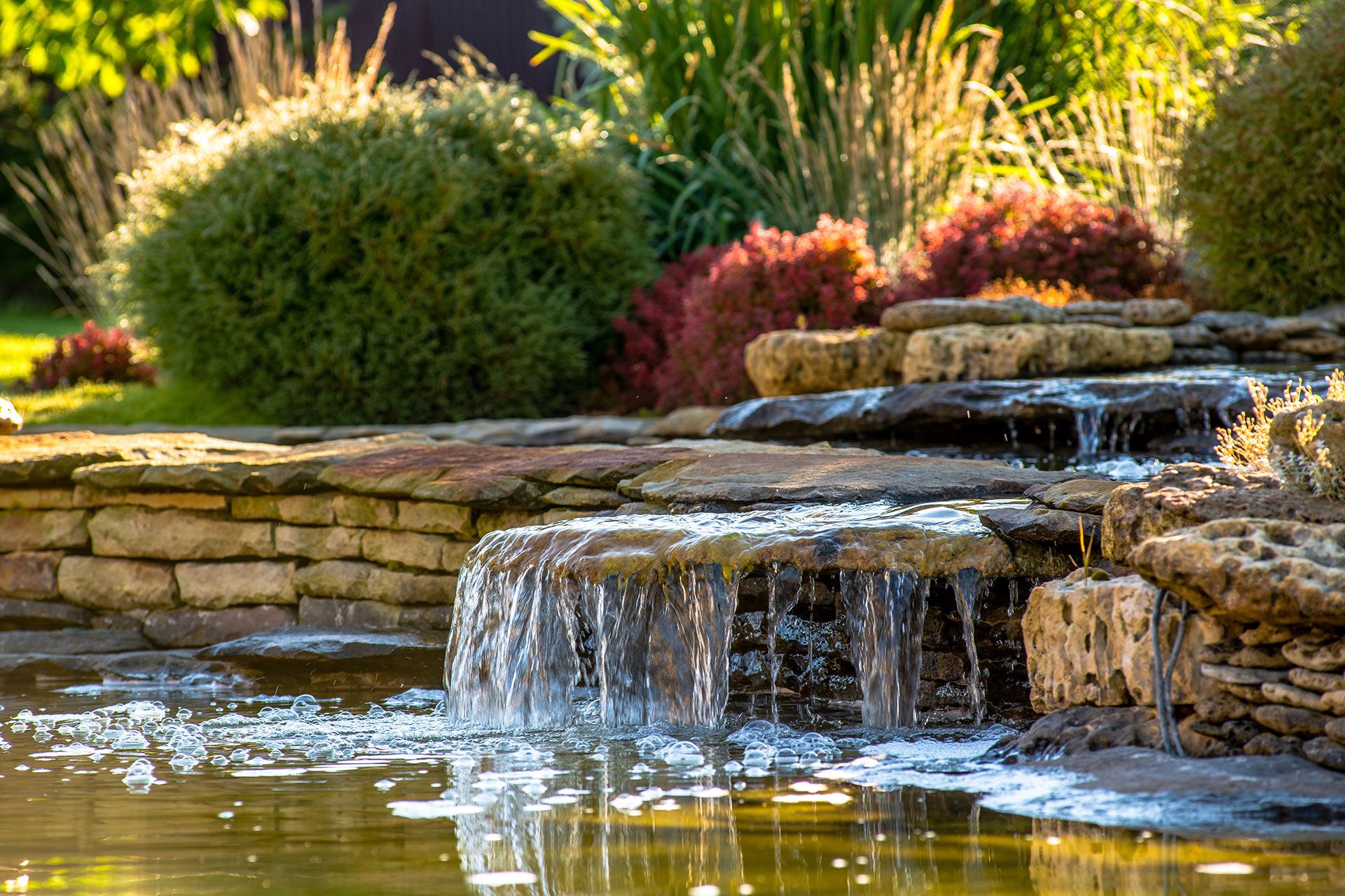 Waterfall cascading into a pond, surrounded by lush plants and stone tiers.