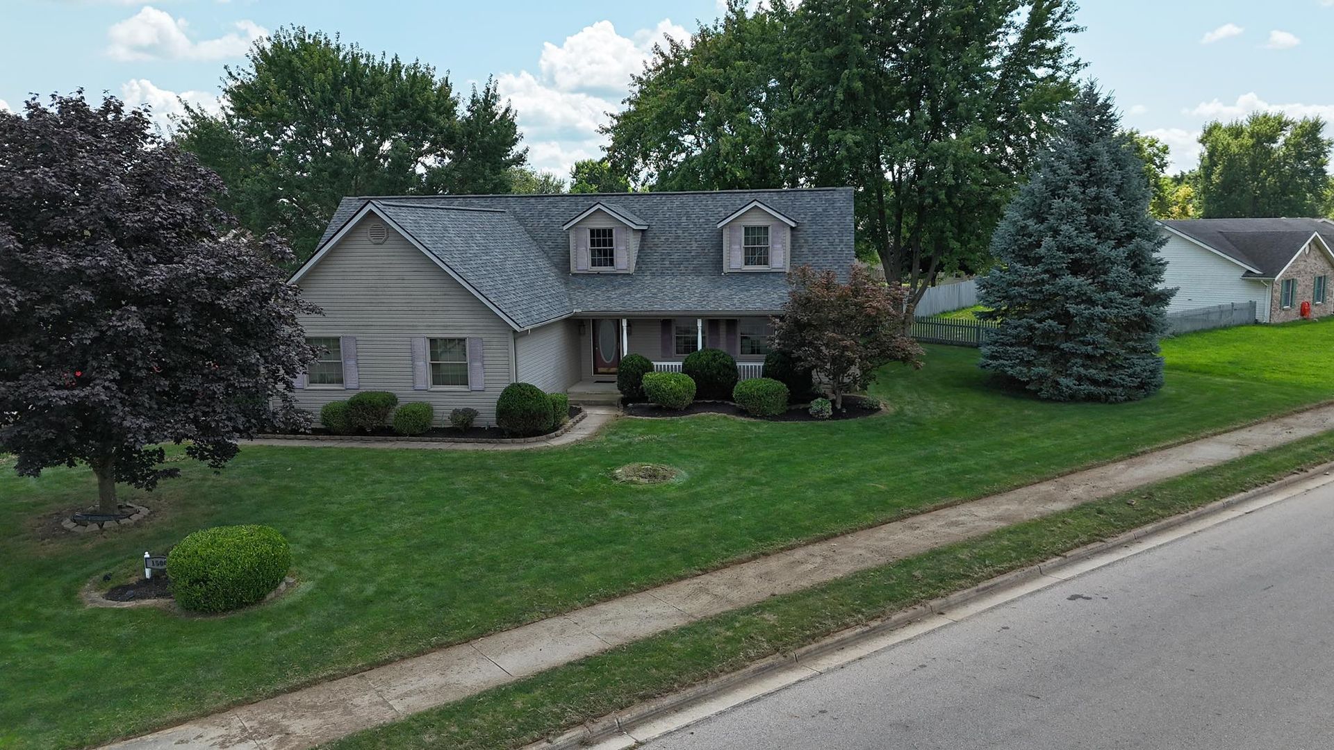 House with a gray roof, lawn, and landscaping. Trees surround the property on a sunny day.