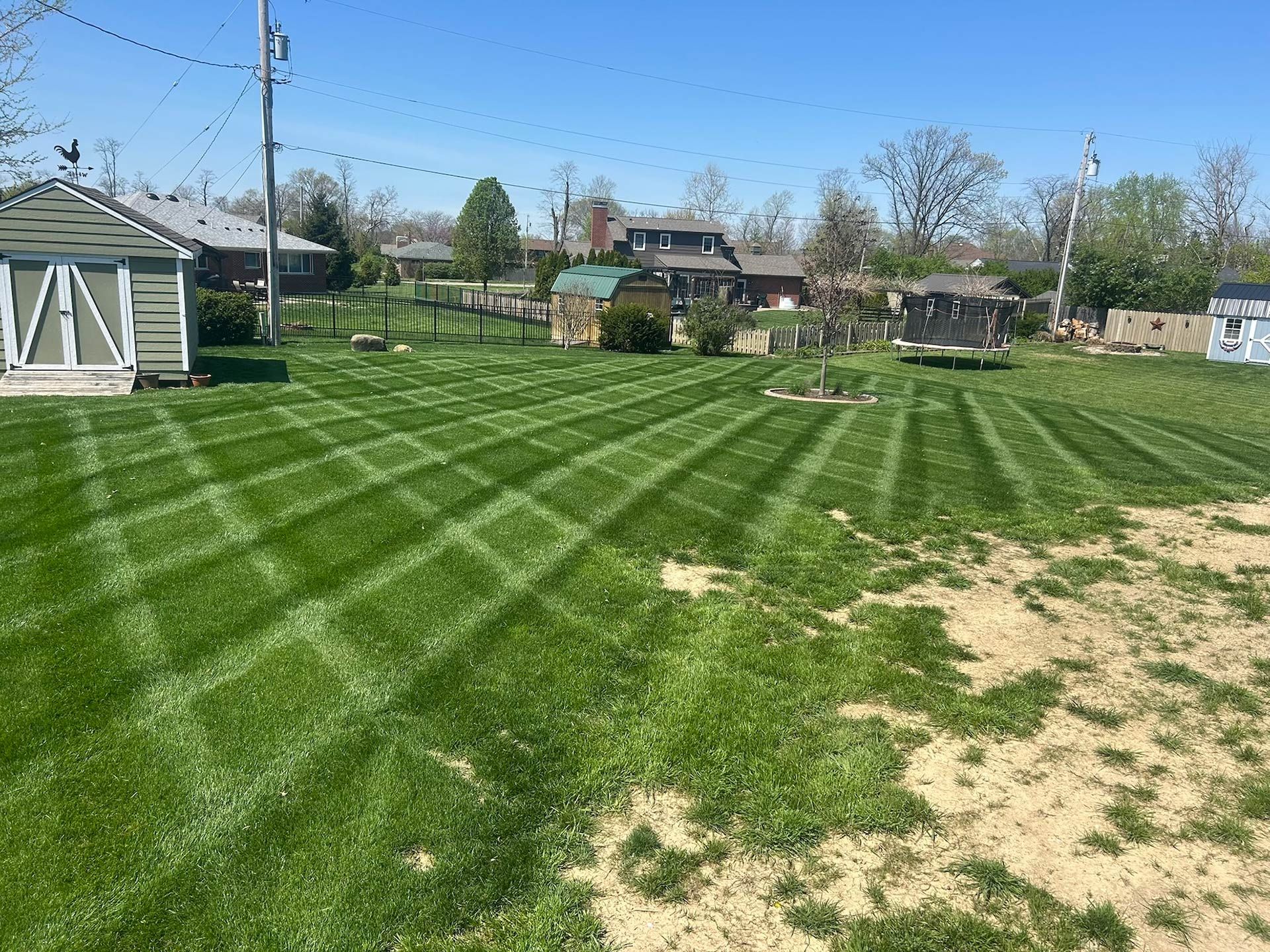 Lawn with a diamond-patterned mowing design; several small buildings in the background. Green grass, blue sky.