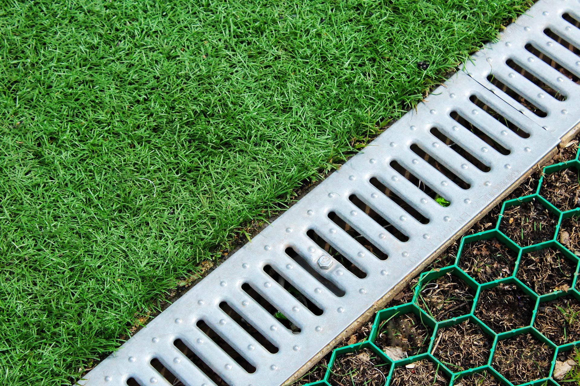 Metal drain next to green grass and a green honeycomb ground grid.