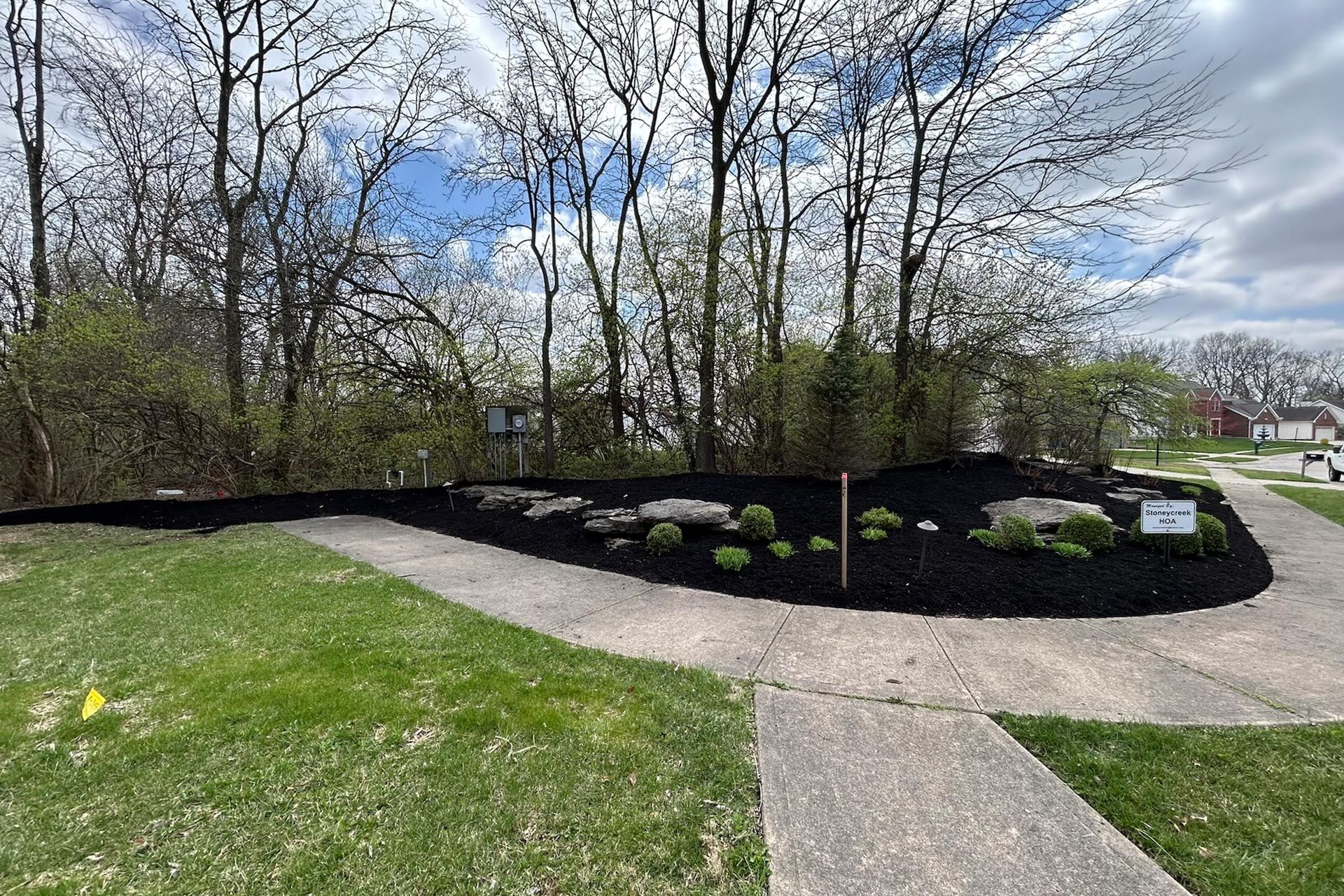 A landscaped island with black mulch, rocks, and small plants next to a concrete walkway and green lawn.