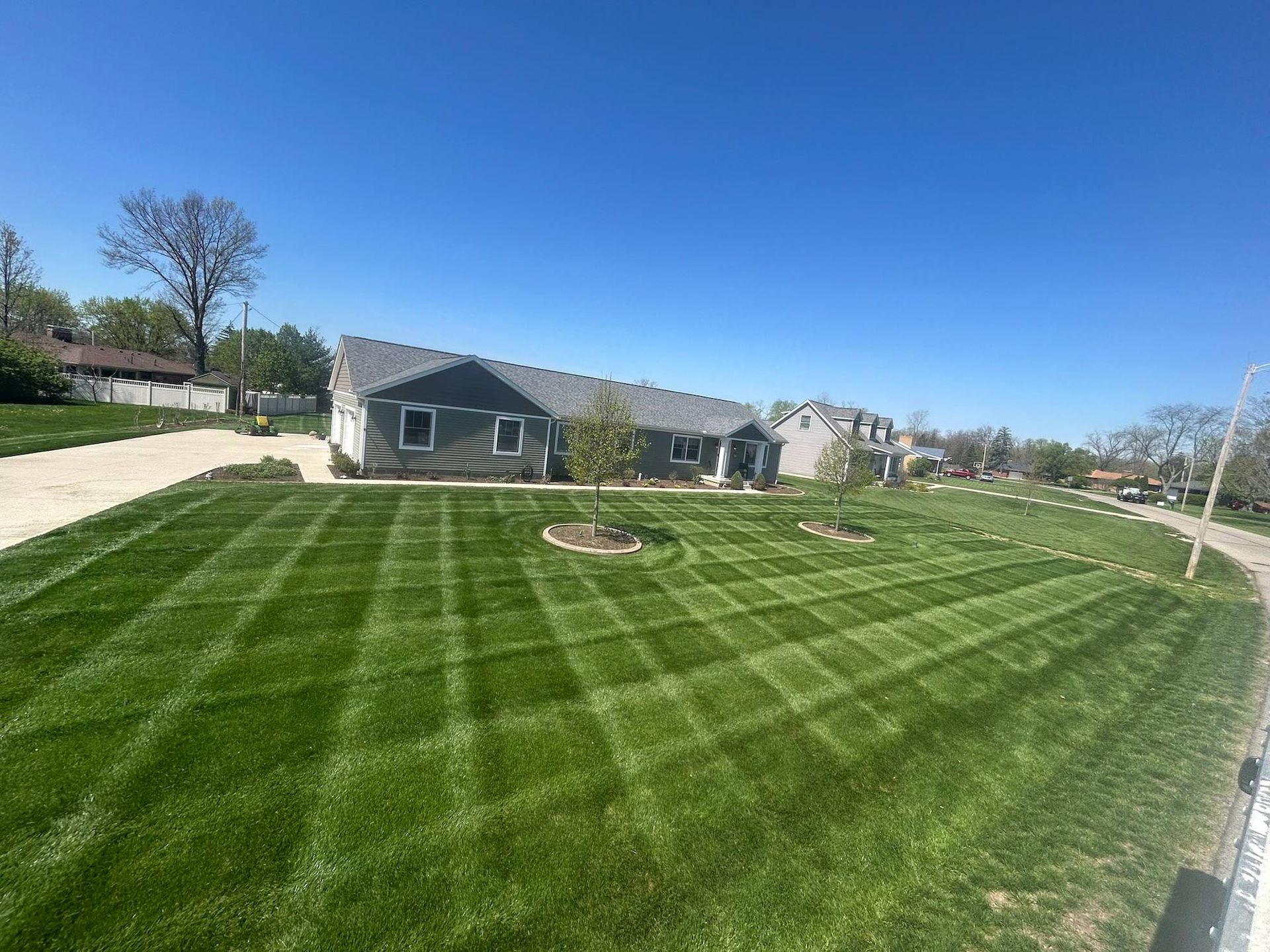 Lawn with a checkered mowing pattern in front of a gray house under a blue sky.