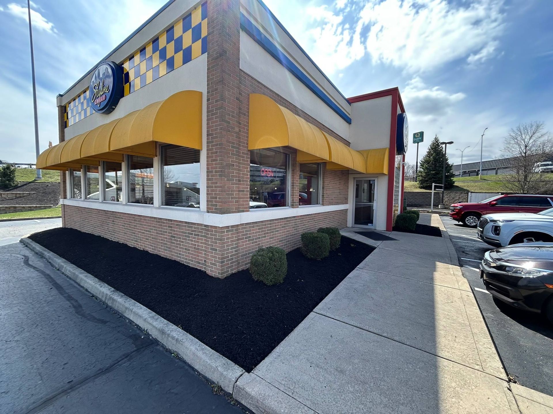 Exterior of a restaurant with yellow awnings, checkerboard accents, and a parking lot with cars.