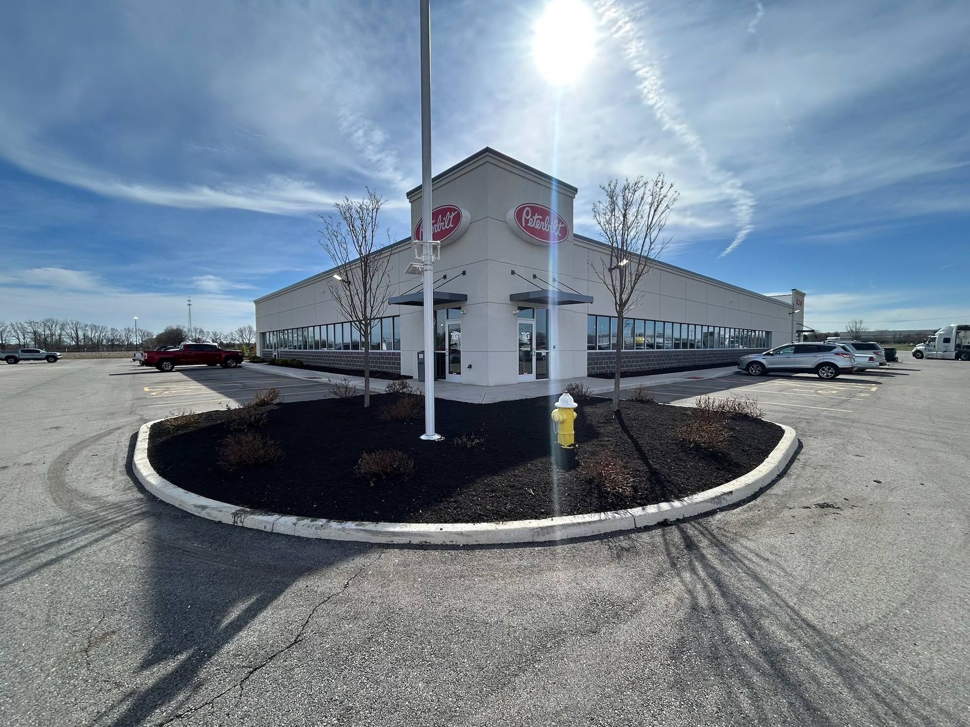 A commercial building with the brand logo. A dark mulch landscaping, a parking lot, and the sun shines above.