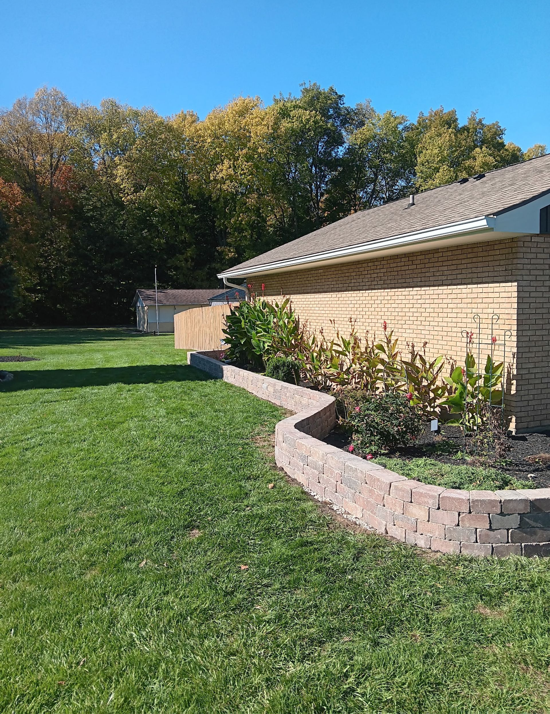 Brick retaining wall with plants in front of a tan brick house on a sunny day.