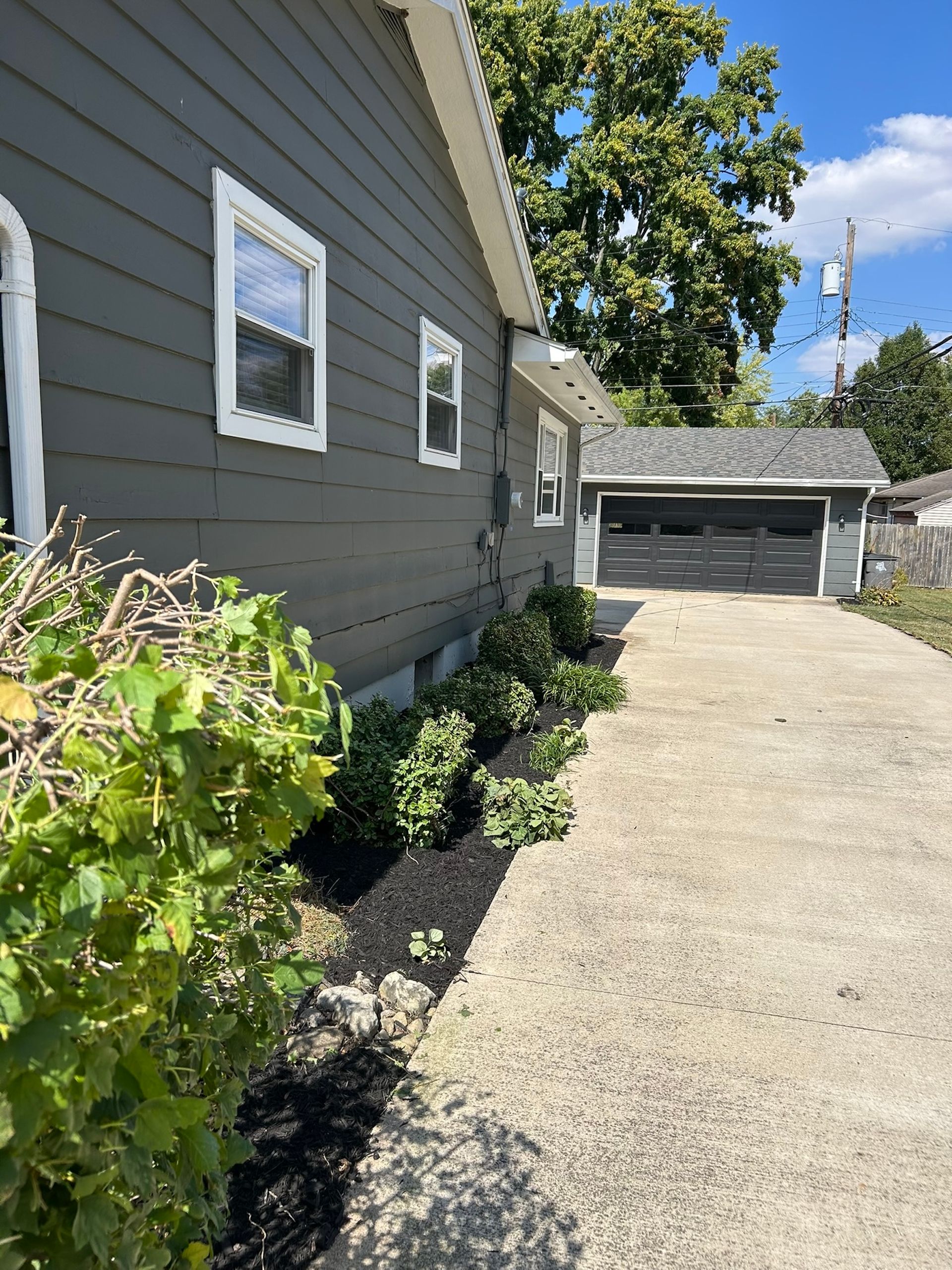 Gray house with a driveway and small garden beds lined with black mulch.