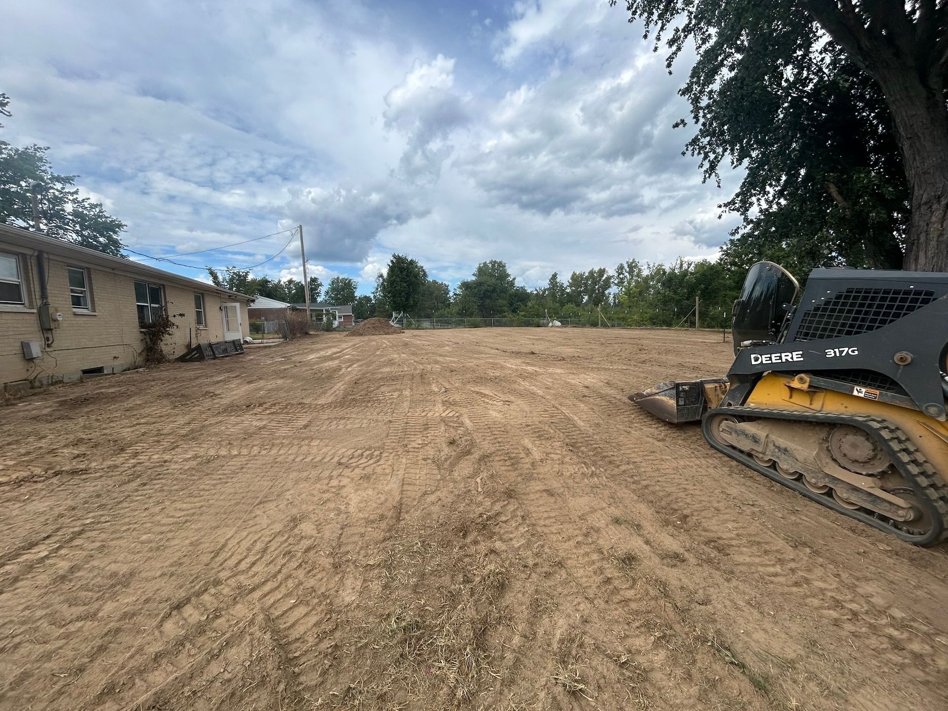 A leveled dirt lot with a small skid steer on the right side and a building on the left.