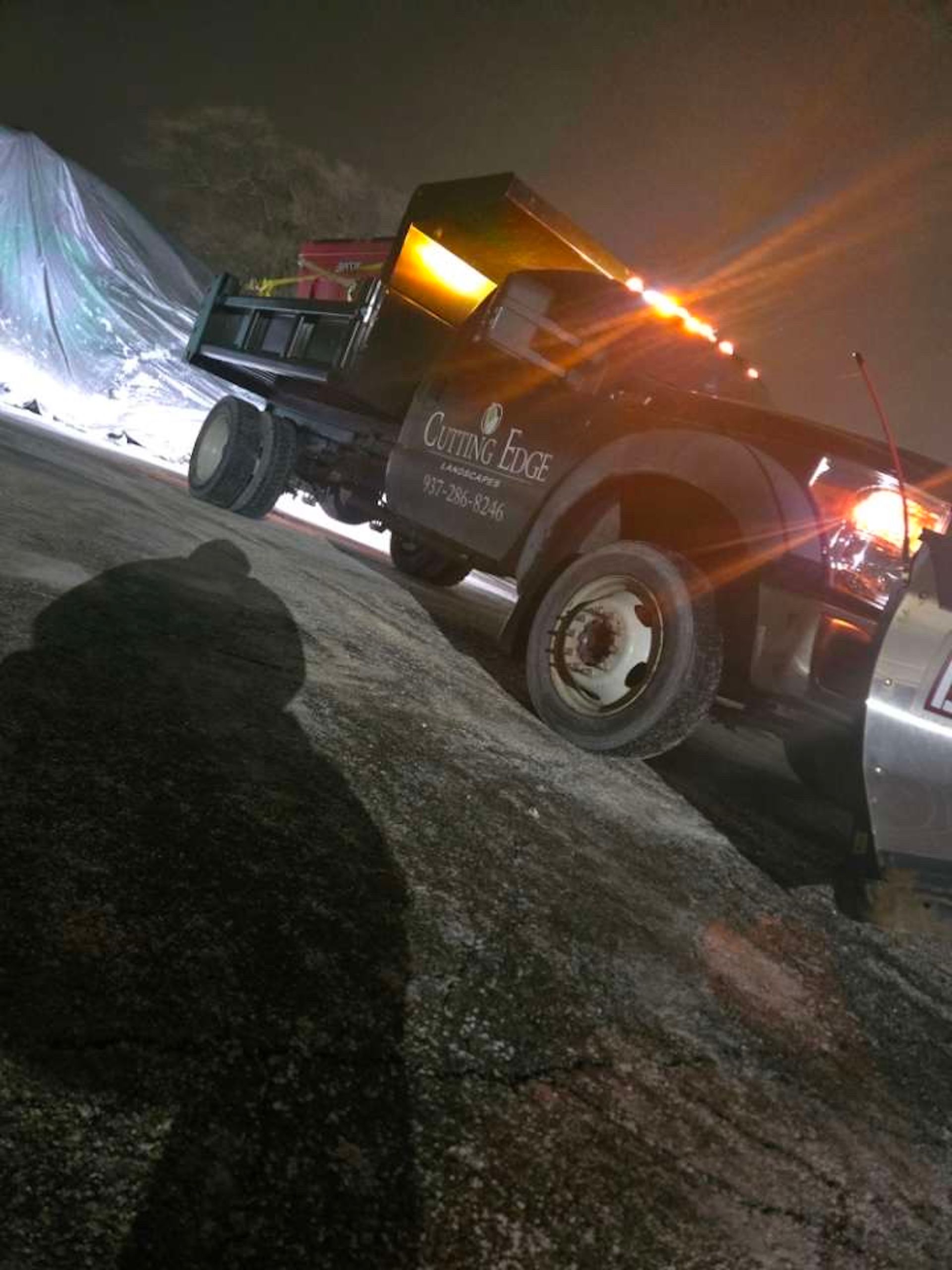 Black dump truck angled on a snow-covered hill at night, illuminated by its lights.