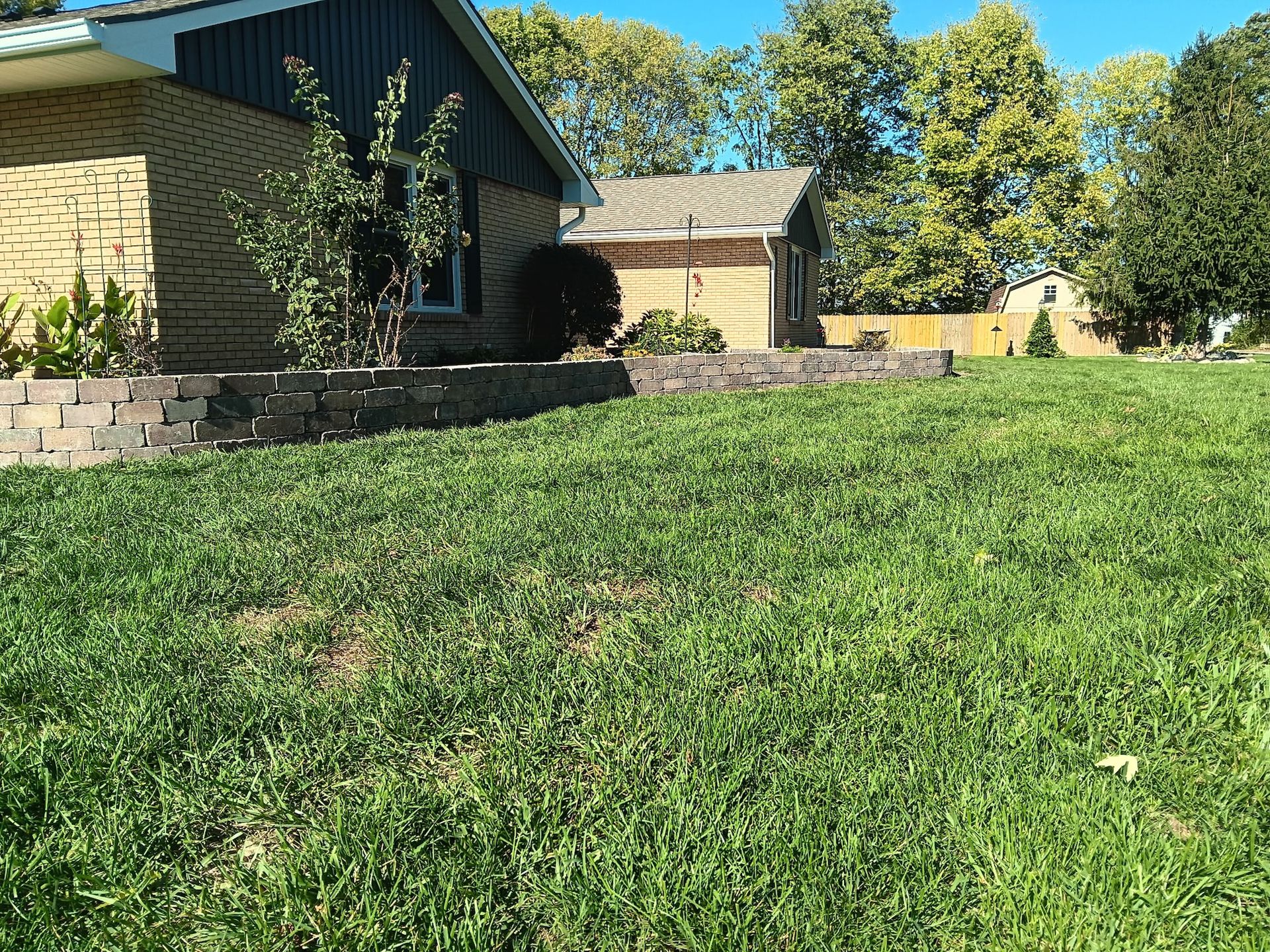 Aerial view of a house with a green lawn, gardens, and surrounding farmland.