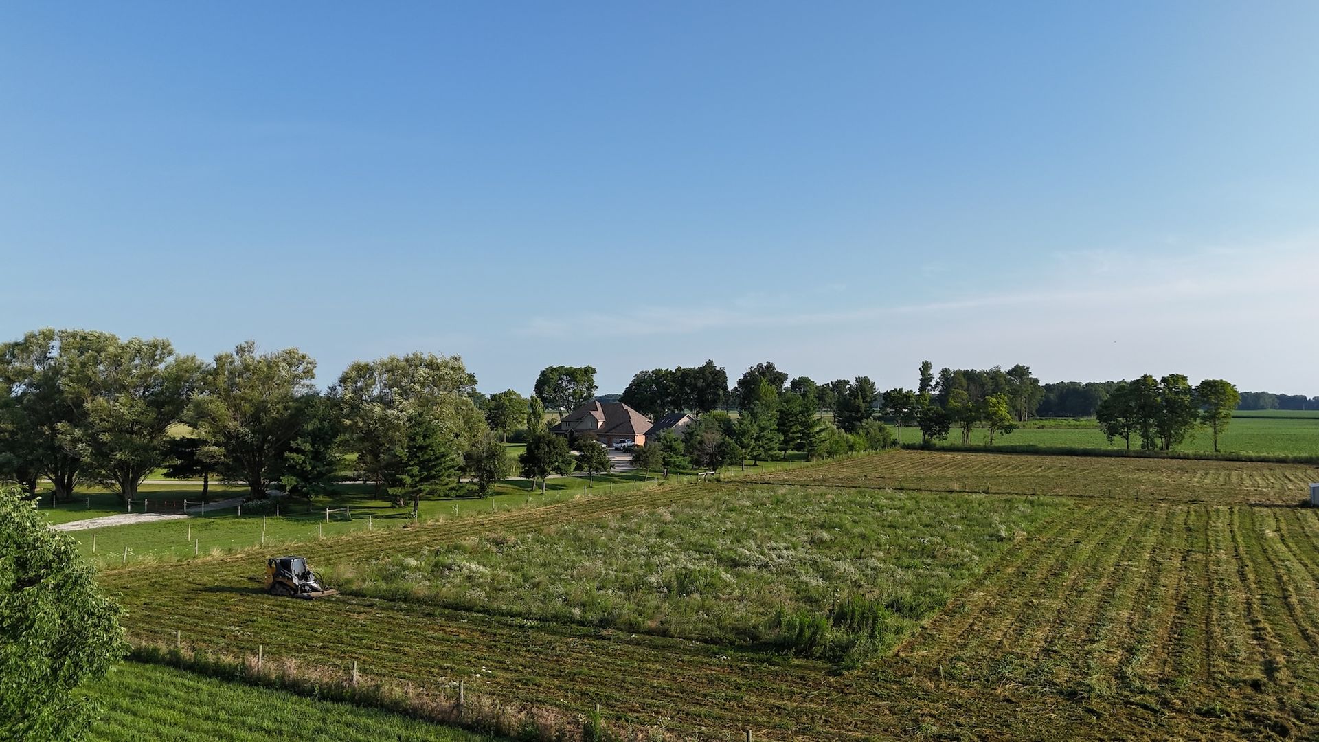 Farm field with trees and a house under a clear blue sky.