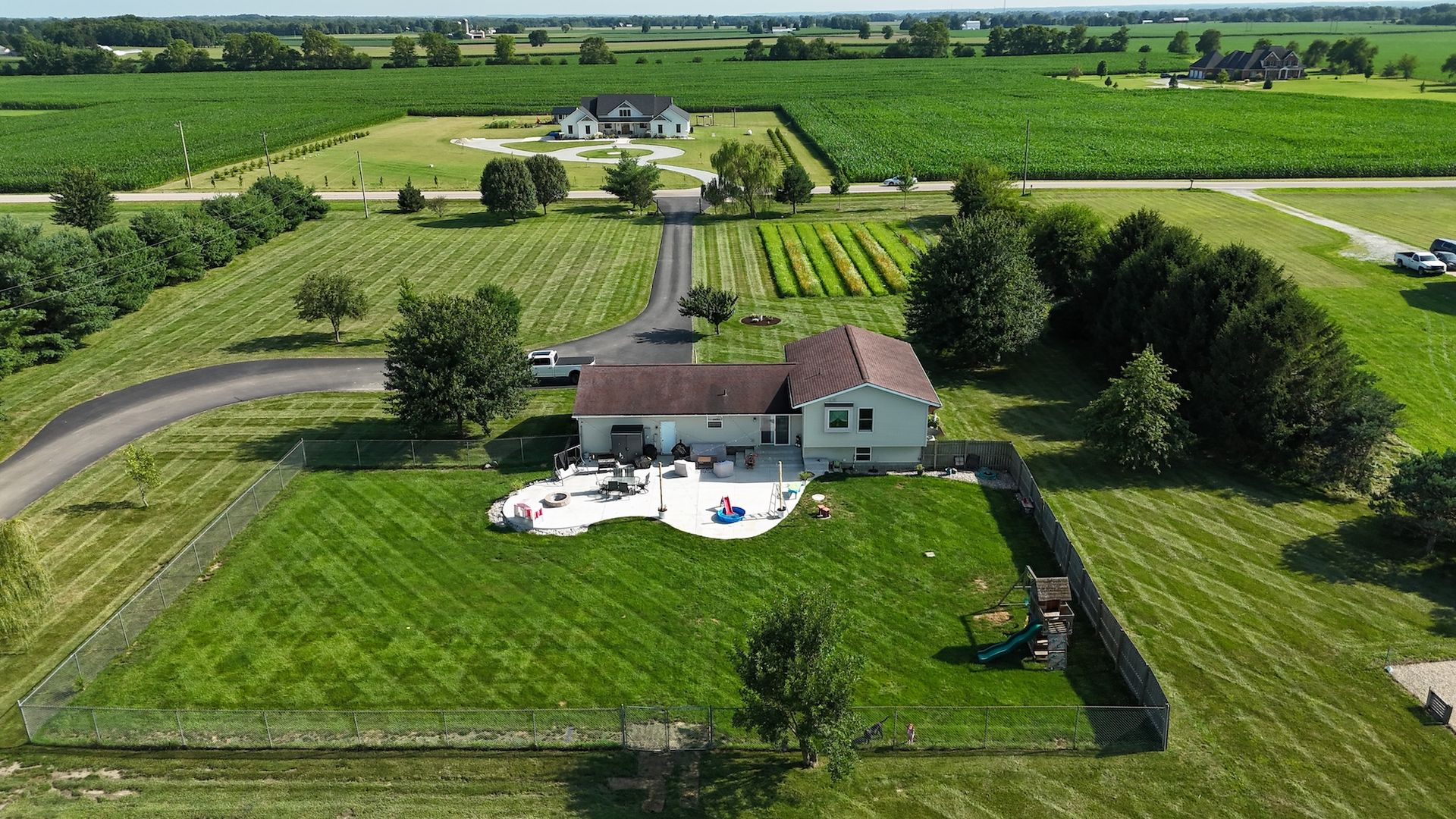 Aerial view of a house with a green lawn, garden, and surrounding farmland.