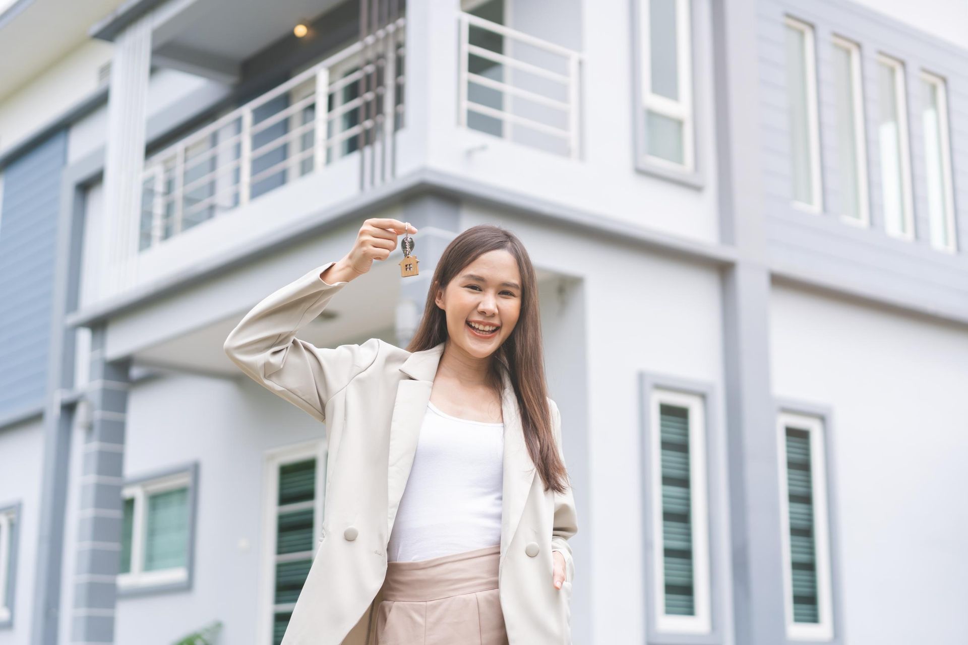 A woman is holding a key in front of a house.