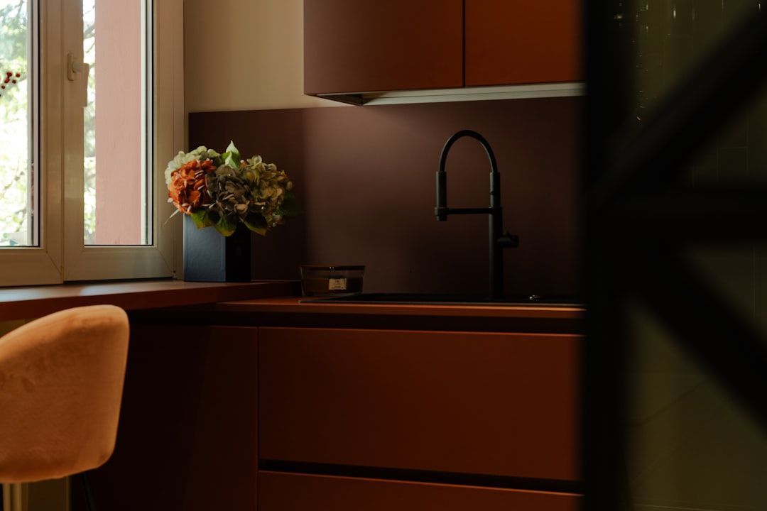 A modern kitchen with dark orange cabinets and backsplash, black faucet, and a bouquet of flowers on the counter.